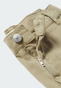 Pantaloni in cotone beige con chiusura a zip e bottone a pressione di colore argento, con tessuto testurizzato e dettaglio della vita piegata.