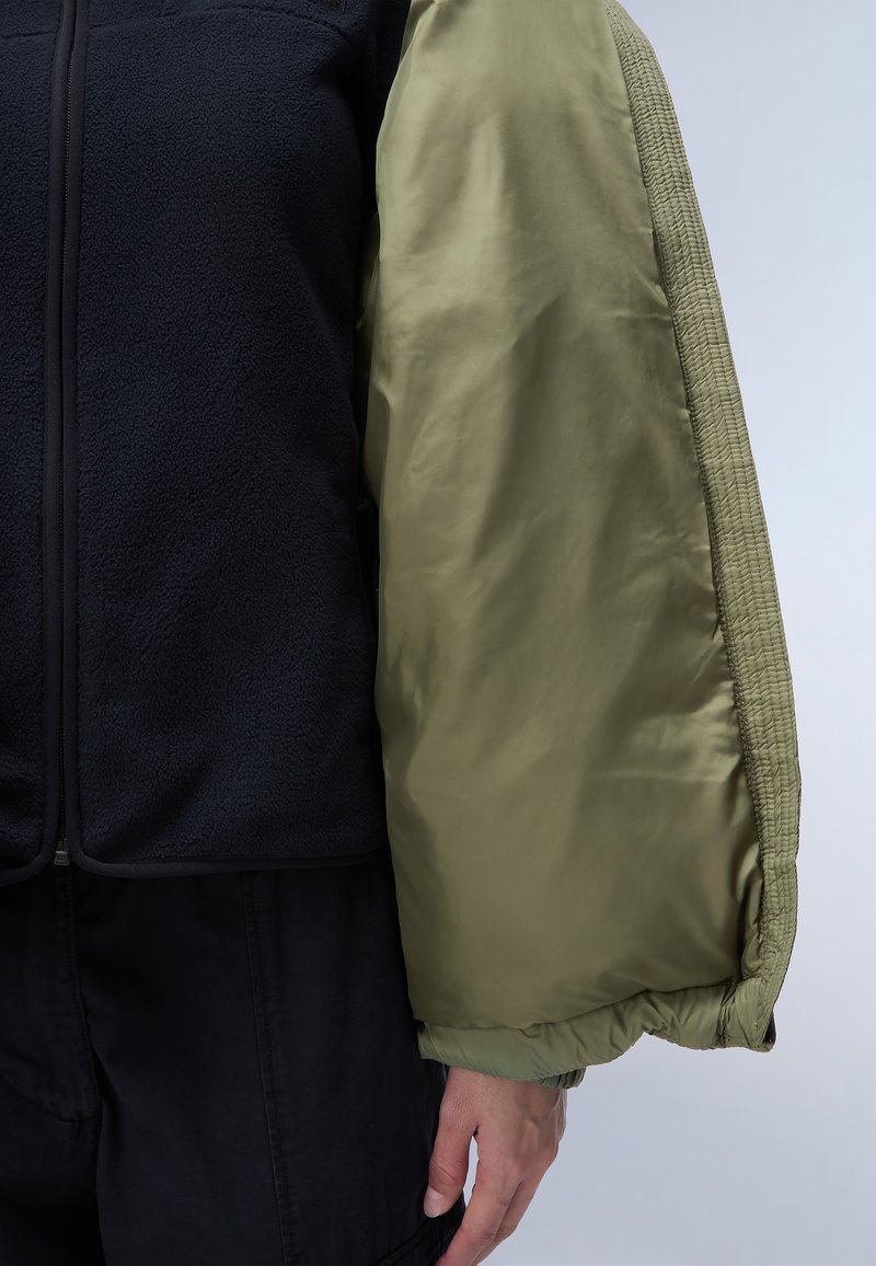 Chaleco de forro polar negro con mangas acolchadas brillantes de color verde oliva. Presenta puños elásticos y una cremallera suave en el centro frontal.