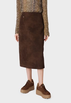 Falda midi de ante marrón combinada con zapatillas marrones con plataforma y forro de piel en una persona que lleva una camiseta de manga larga con estampado.