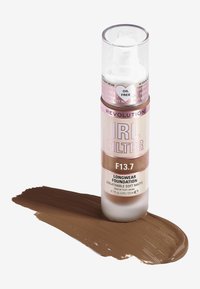 Langvarig foundation i en gjennomsiktig pumpeflaske. Lys beige til middels brun nyanse, merket "F13.7," med en glatt, blank overflate.