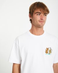 T-shirt en coton blanc à manches courtes. Présente un graphique coloré d'un chat et d'une chope de bière sur la poitrine gauche. Texture douce, coupe décontractée.