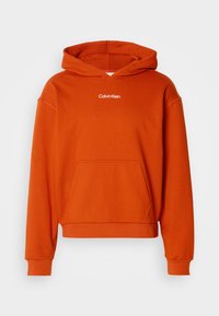 Felpa arancione con cappuccio, dotata di tasca frontale e logo "Calvin Klein" bianco sul petto. Realizzata in tessuto morbido e texturizzato.