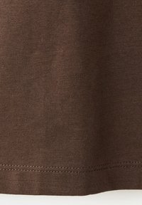 Gros plan sur un tissu marron avec des coutures visibles le long du bord inférieur, montrant la texture et le motif tricoté.