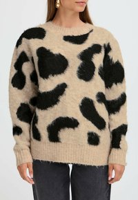 Pull en laine beige avec un imprimé léopard abstrait noir, poignets et ourlet côtelés, texture douce et coupe décontractée.