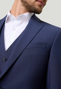 Nahaufnahme des Oberkörpers eines Mannes in einem maßgeschneiderten marineblauen Anzug mit einem weißen Hemd, das die Details und die Textur des Anzugs zeigt.