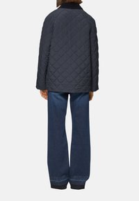 Veste matelassée bleu marine avec un col montant, associée à un jean en denim bleu à jambe large. La veste présente un motif en losanges et une coupe décontractée.