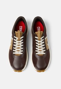 Sneaker marrone con parte superiore in mesh e sintetico, lacci bianchi, accenti beige, soletta rossa e suola in gomma crema con impugnature circolari testurizzate.