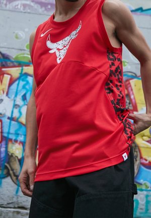 Maillot de sport sans manches rouge avec texture en maille, présentant un graphisme de taureau et des accents géométriques noirs sur les côtés.