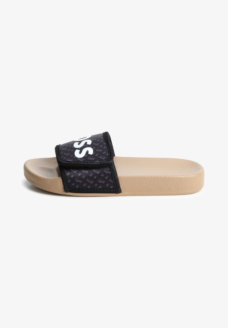 Sandale beige à enfiler avec semelle texturée et bride noire réglable avec un texte blanc partiellement en gras.