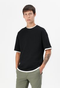 T-shirt noir à manches courtes avec un col et des poignets en côte blanche. Présente une coupe décontractée et est fabriqué en coton doux.