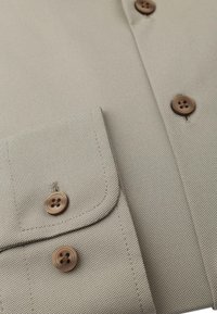 Beige overhemd met een gestructureerde oppervlakte, voorzien van twee bruine knopen en een zak aan de linkerkant. Gladde stof en op maat gemaakte ontwerpelementen.