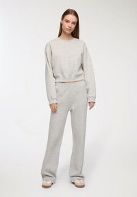 Felpa grigia oversize con maniche lunghe, abbinata a pantaloni larghi coordinati. Il materiale sembra morbido; l'outfit ha una vestibilità rilassata.