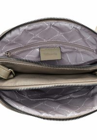 Interno della borsa beige con due scomparti con zip, rivestimento a motivo grigio chiaro e un'etichetta cucita visibile all'interno.