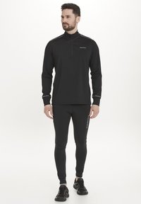 Sort langærmet atletisk top med lynlås, parret med tætsiddende sorte leggings med hvide sidedele. Båret med sorte atletiske sko.