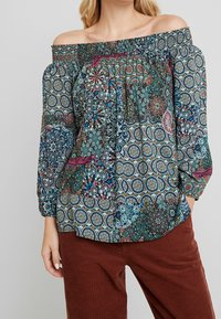 Olkapäiltä avonainen paita, jossa on monivärinen kuvio, joka koostuu pyöreistä ja kukkamaisista muodoista. Paitassa on joustava kaula-aukko ja pitkät pöhöttävät hihat.