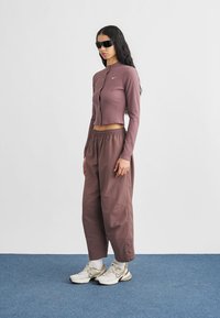 Ριμπ, κοντοκομμένο τοπ σε μαύρο μαύρο με μακριά μανίκια και κουμπιά στο μπροστινό μέρος; φαρδιά μαύρα παντελόνια; λευκά αθλητικά παπούτσια με ασημί λεπτομέρειες; μαύρα γυαλιά ηλίου.