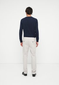 Cămașă albastră cu mânecă lungă, asociată cu pantaloni bej deschis. Pantalonii au buzunare posterior cu nasturi și un design slim fit. Pantofii negri completează ținuta.
