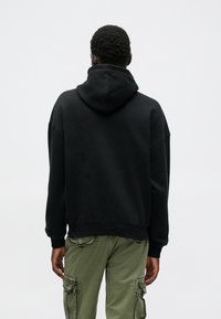 Μαύρη φούτερ μπλούζα με κουκούλα σε χαλαρή γραμμή, συνδυασμένη με ελαιόχρωμα cargo παντελόνια με τσέπες. Μαλακό, υφή ύφασμα.