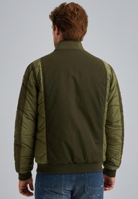 Veste bomber verte olive avec des manches matelassées, un col et des poignets côtelés, et une taille ajustée. Présente une poche sur le bras gauche.