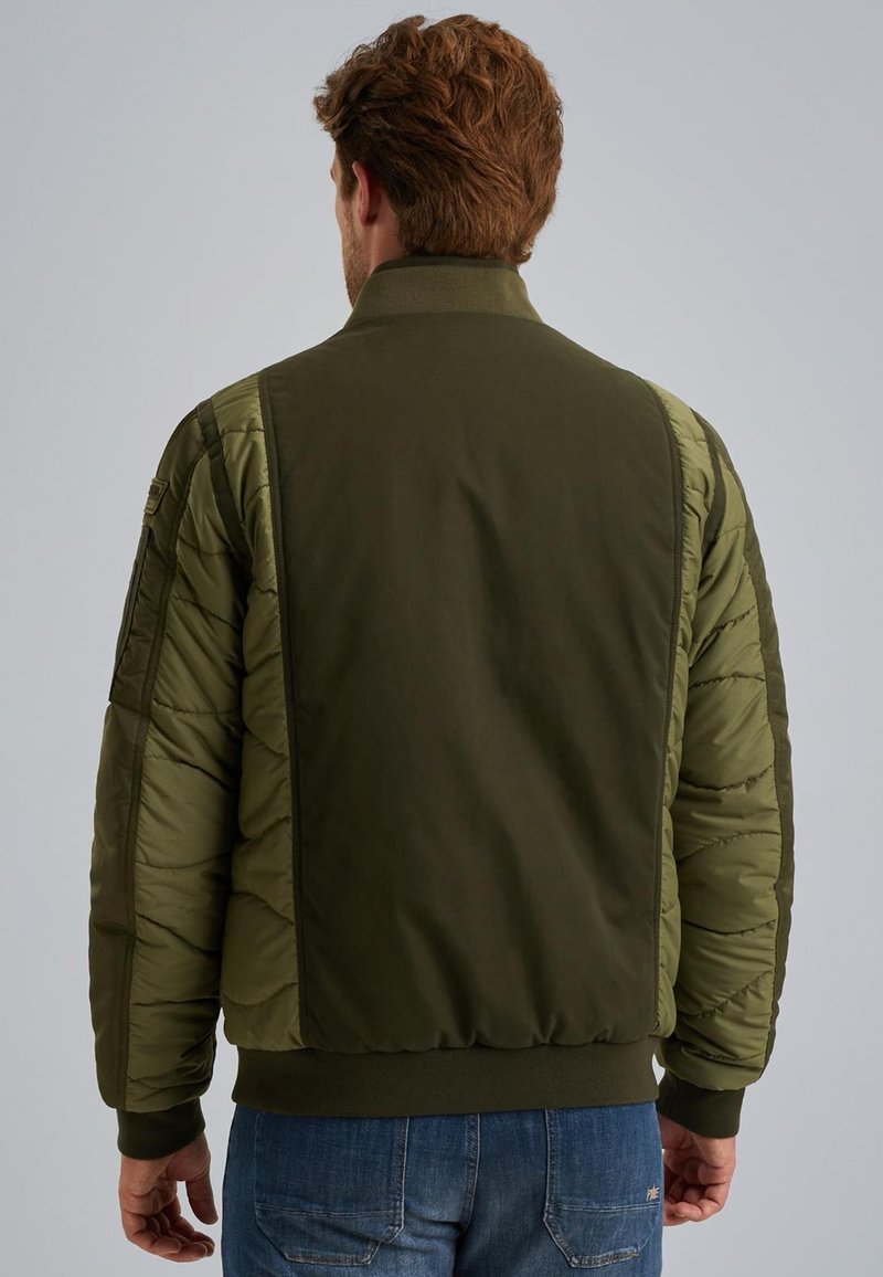 Veste bomber verte olive avec des manches matelassées, un col et des poignets côtelés, et une taille ajustée. Présente une poche sur le bras gauche.