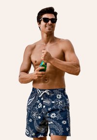 Shorts da nuoto navy con motivi floreali e paisley bianchi, vita con cordoncino e vestibilità comoda; il tessuto appare liscio e leggero.