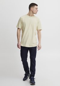 Tricou din bumbac galben deschis, cu mâneci scurte, croială lejeră, decolteu rotund. Asortat cu blugi negri și pantofi sport negri.