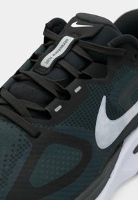 Baskets noires et bleu sarcelle foncé avec dessus en mesh, accents gris et logo swoosh blanc. Caractérisées par des lacets et une semelle rembourrée.