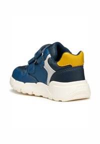 Zapatilla azul y amarilla con parte superior de sintético texturizado, suela blanca, correas de Velcro y un acento plateado en contraste en el costado.