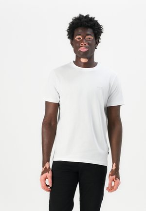 White cotton t-shirt with crew neckline and short sleeves, featuring a subtle logo on the chest, worn with black pants.