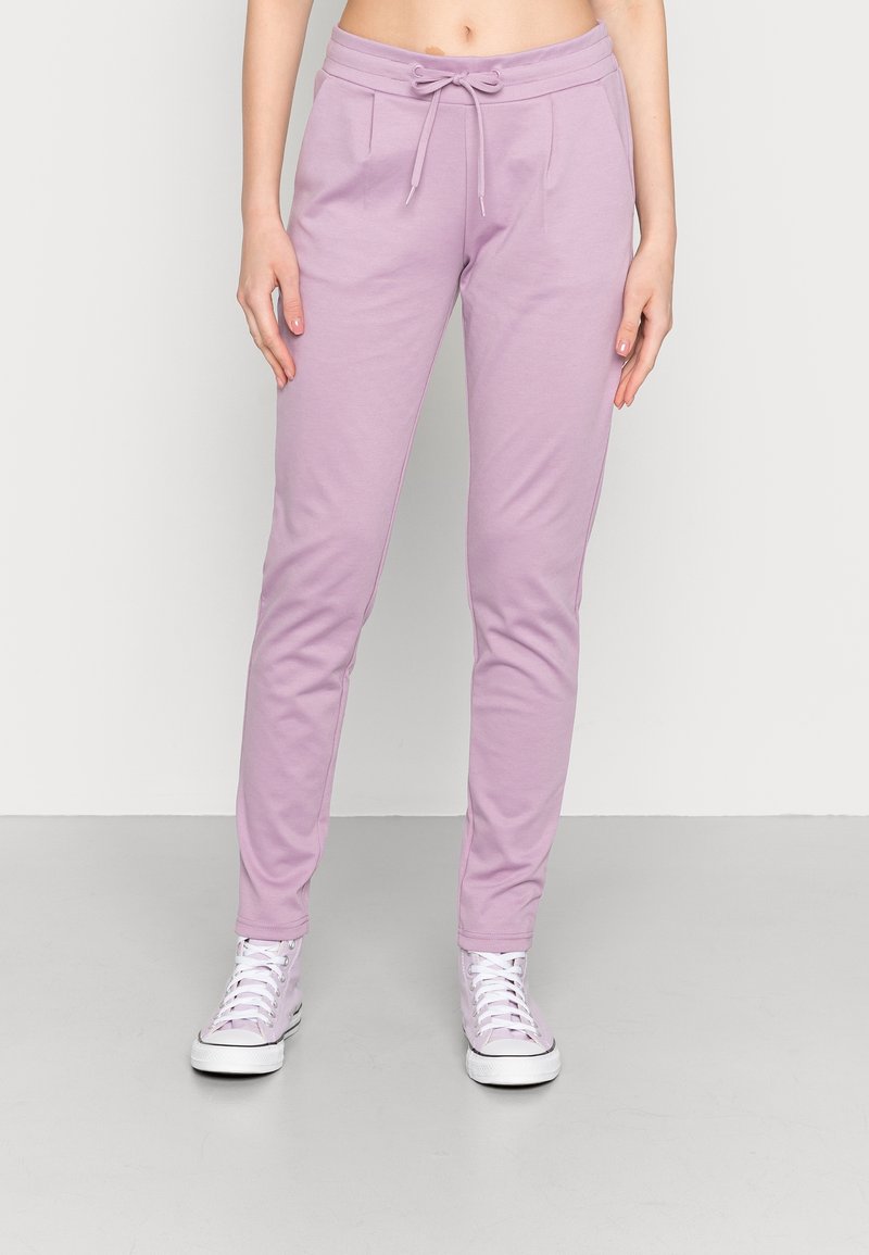 Joggings roses clairs en tissu doux, avec une taille à cordon, des poches latérales et des jambes fuselées, associés à des baskets blanches.