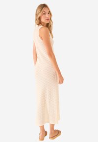Robe sans manches de longueur genou en beige clair, arborant un motif en zigzag et une texture côtelée, assortie à des sandales marron clair.