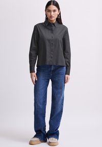 Donkergrijze button-up shirt met een kraag, lange mouwen en een rechte snit. Gecombineerd met blauwe spijkerbroek en beige schoenen.