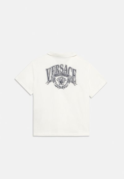 Άσπρο κοντομάνικο πόλο μπλουζάκι με το κείμενο "VERSACE", το λογότυπο με το κεφάλι της Μέδουσας και τη σημαία "Established 1978" τυπωμένα στην πλάτη.