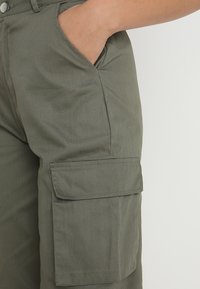 Oliivinvihreät cargo-housut, joissa on tasku reidessä, valmistettu kestävästä puuvillakankaasta, jossa on rento istuvuus ja siistit linjat.