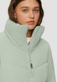Jasnozielona, pikowana kurtka z wysokim kołnierzem, wykonana z teksturowanego, karbowanego materiału, z zapięciem na zamek błyskawiczny oraz materiałową pętelką.