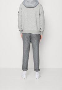 Grijze sweatshirt met een lichtgrijze capuchon, gecombineerd met grijze geruite broek, opgerold bij de boorden. Witte schoenen maken de outfit compleet.
