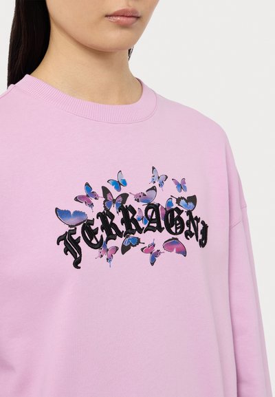 Vaaleanpunainen huppari, jossa on kukkakuvioista perhospainatus sinisenä ja purppurana sekä musta teksti. Ribbauskankaasta valmistettu pyöreä kaula-aukko, rento malli.