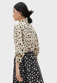 Blusa beige con pois neri, vestibilità ampia e maniche leggermente a sbuffo. Gonna blu marina con un motivo simile, legata in vita.
