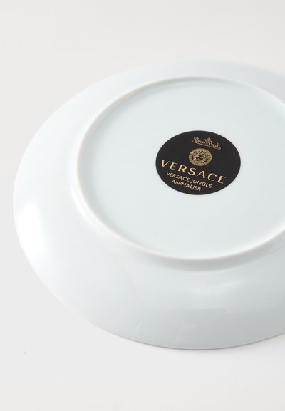 Ανοιχτό μπλε πορσελάνινο πιάτο με γυαλιστερό φινίρισμα, που διαθέτει μαύρη ετικέτα με χρυσό κείμενο "Versace Jungle Animalier".