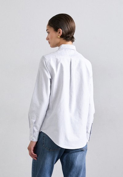 Chemise à rayures bleu clair et blanche. Comprend des manches longues, un ourlet arrondi et un pli dans le dos pour plus de liberté de mouvement.