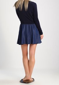 Dark blue skater dress with a fitted long-sleeve top and flared denim skirt. Flat sandals with a cork footbed. Smooth fabric texture.
