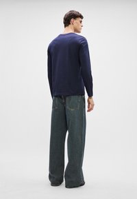 Mornarsko modra majica z dolgimi rokavi v kombinaciji z ohlapnimi temno modrimi kavbojkami. Majica ima zaobljen izrez in je preprosta zasnova.