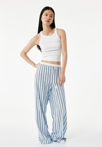 Ljusblå randiga vida byxor med dragsko i midjan och mjukt tyg, kombinerat med en vit ribbad linne.