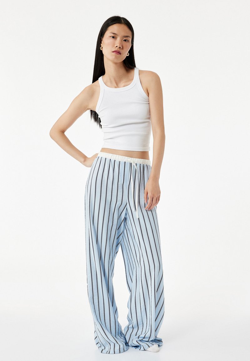 Ljusblå randiga vida byxor med dragsko i midjan och mjukt tyg, kombinerat med en vit ribbad linne.