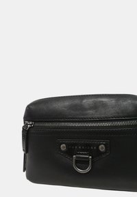 Borsa nera in pelle con chiusura a zip, caratterizzata da una placca con logo argento e dettagli in metallo. Texture liscia e forma rettangolare.