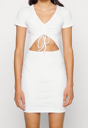 Femme portant une robe courte à manches courtes en maille côtelée blanche avec un col en V, un lien froncé à l'avant et une découpe au niveau du ventre.