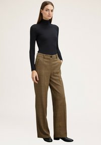 Schwarzes Rollkragenoberteil mit langen Ärmeln, kombiniert mit braunen karierte weit geschnittenen Hosen mit hoher Taille und Seitentaschen. Schwarze Stiefel mit Absatz.