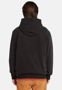 Felpa nera con una texture liscia, dotata di un cappuccio con cordino e polsini a costine. Posizionata sopra una maglietta rossa; vista posteriore.