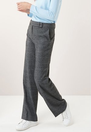 Pantalons gris à motifs avec une coupe décontractée, plis à l'avant et poches latérales ; associés à des baskets blanches et un haut bleu clair.