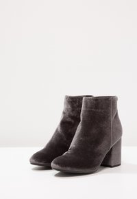 Botines de terciopelo en gris oscuro con un diseño afilado y tacón cuadrado. Textura suave con costuras a lo largo de los bordes.